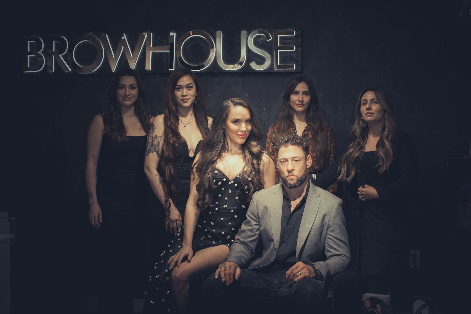 Five stylish professionals pose in front of a Browhouse sign in a dark, elegant studio setting.