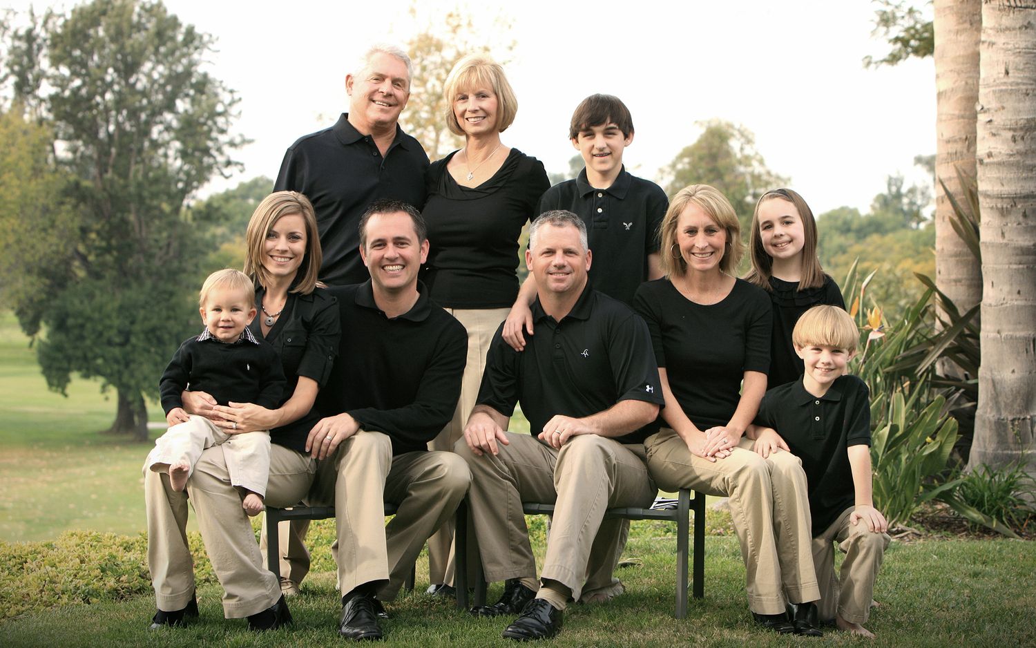 Extended family of nine posing together outdoors in coordinating black and khaki outfits.