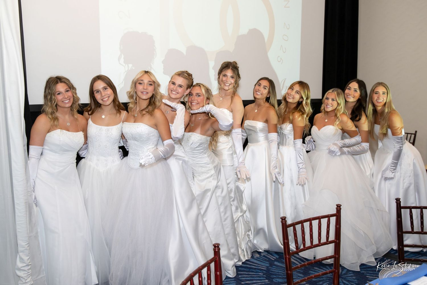 Group of women in elegant white strapless gowns and gloves posing together at a formal debutante ball event.