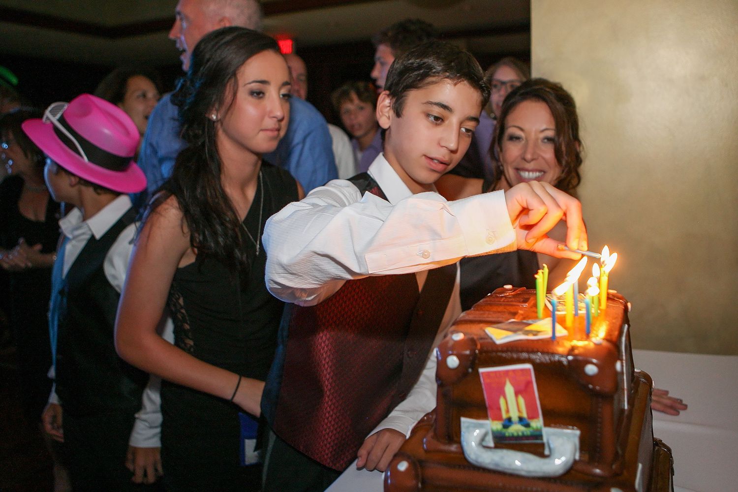 Teen boy lighting candles on a car-shaped birthday cake at a celebration event.