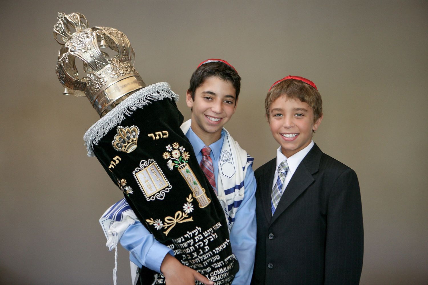 Two boys in formal attire holding a Torah scroll at a Bar Mitzvah ceremony.