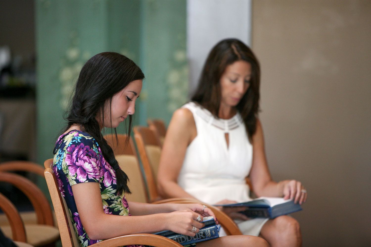 Two women sitting in chairs reading books in a bright indoor setting.