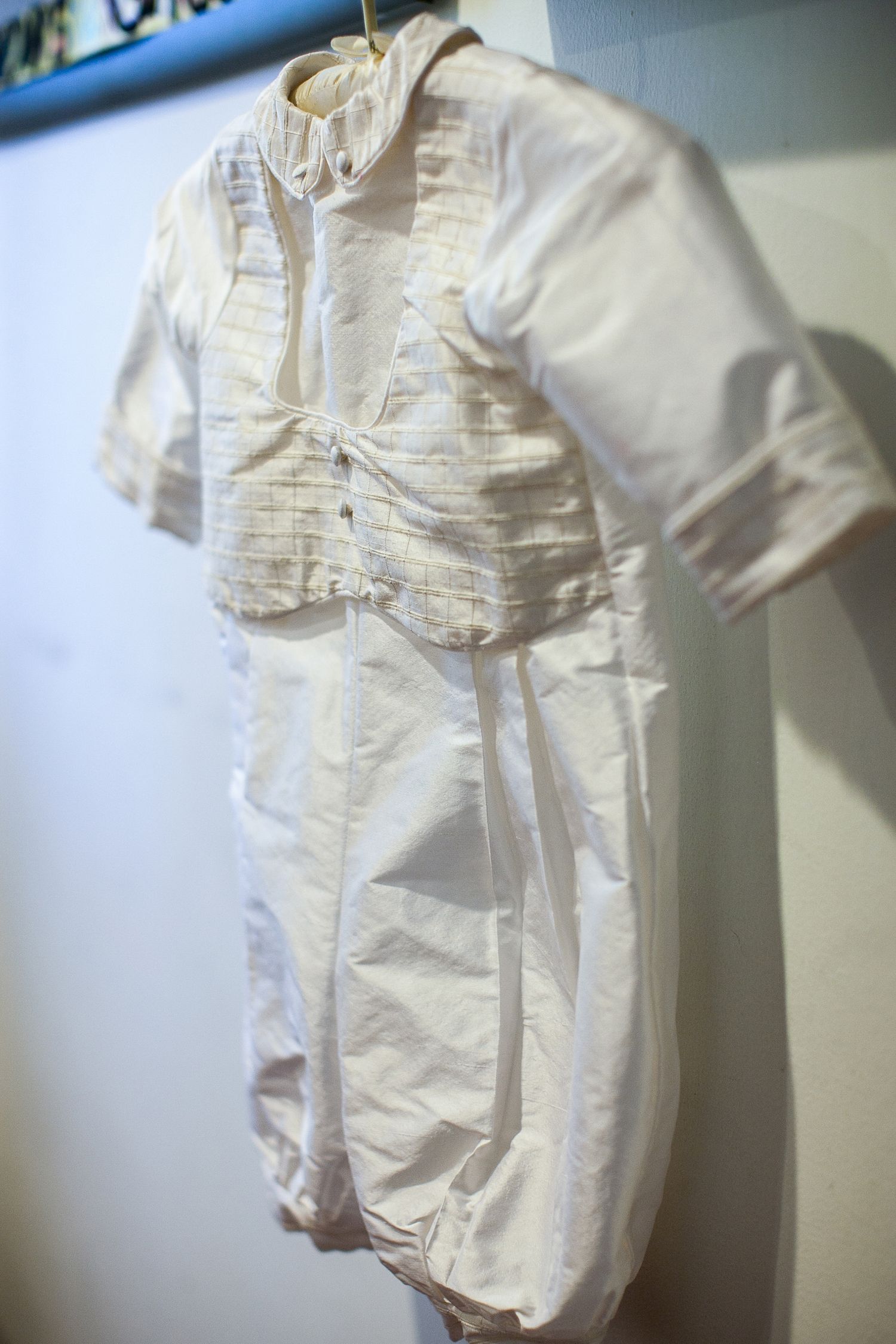 Antique white christening outfit with ruffled collar and pleated bodice displayed on a hanger.