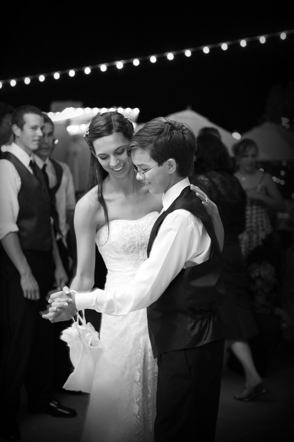 Black and white photo of a smiling bride and groom sharing their first dance at an outdoor wedding reception.