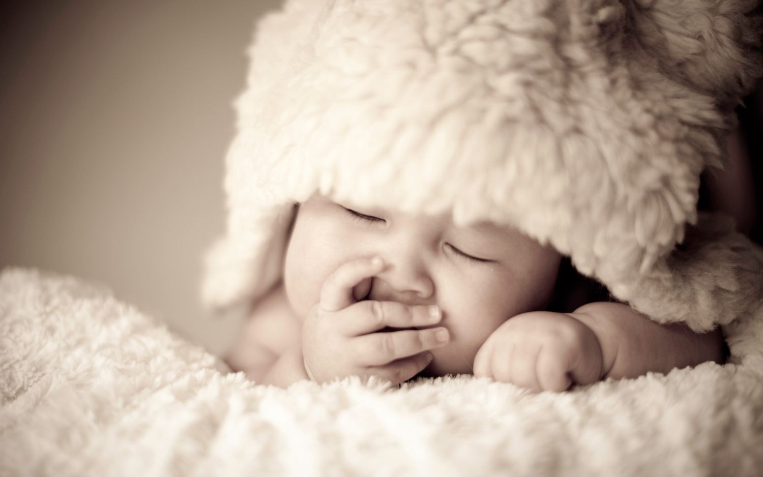 Sleeping newborn baby wearing a fluffy bear hat in sepia tone.
