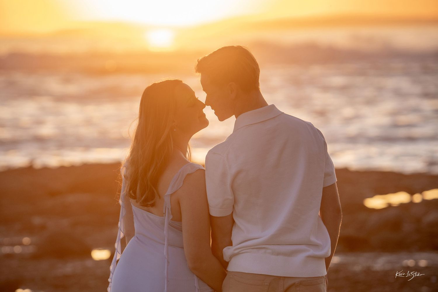Couple facing each other romantically silhouetted against a stunning golden ocean sunset.