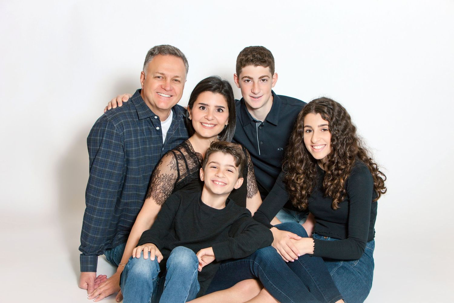 A happy family of five poses together smiling in a professional white studio portrait photo.