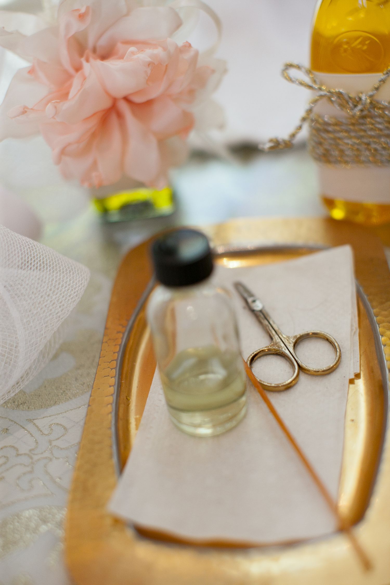 Gold tray with scissors, oil bottle, napkin, pink flowers, and yellow bottles for a manicure setup.
