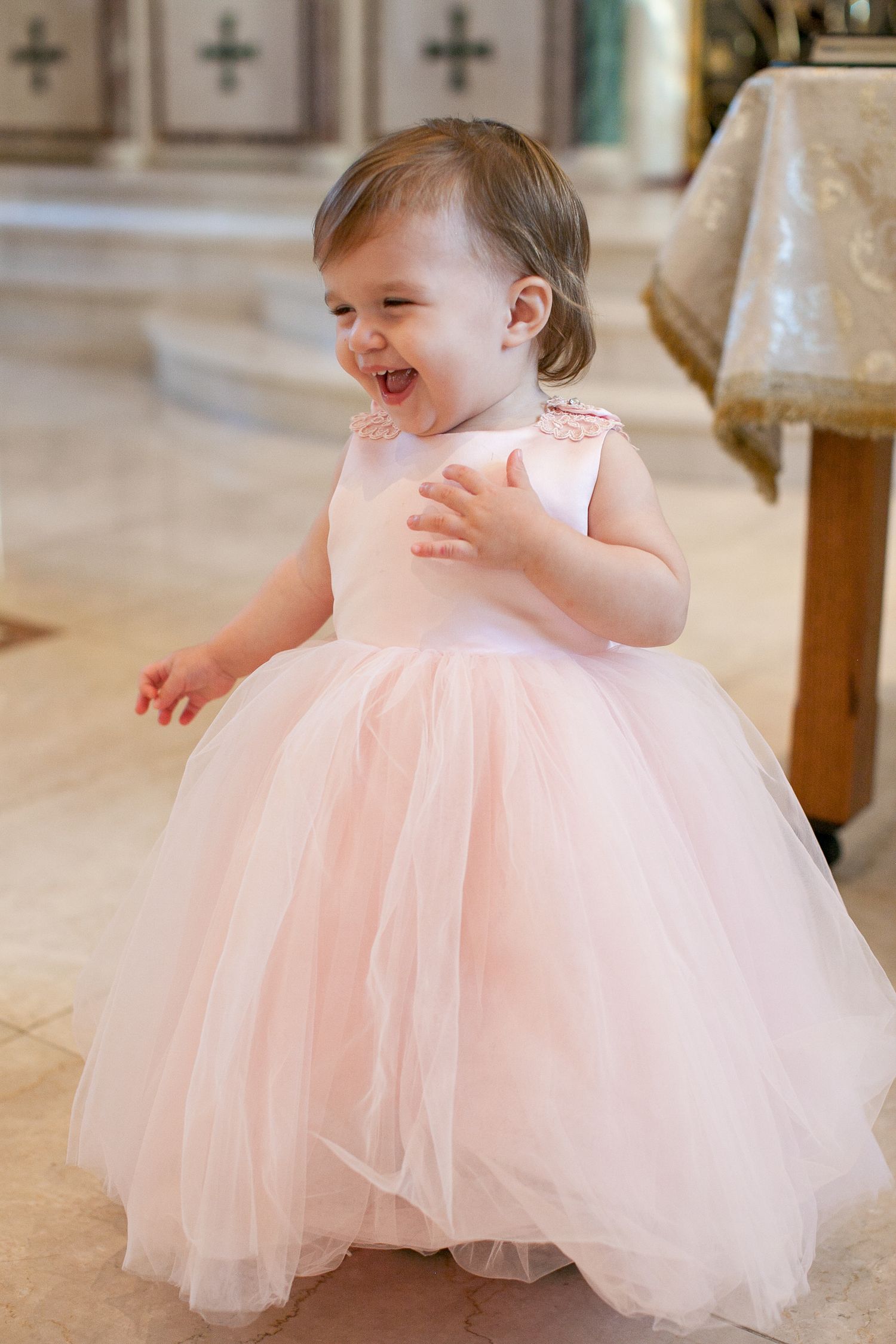 Adorable toddler girl in a pink tulle ball gown dress laughing joyfully inside a church.
