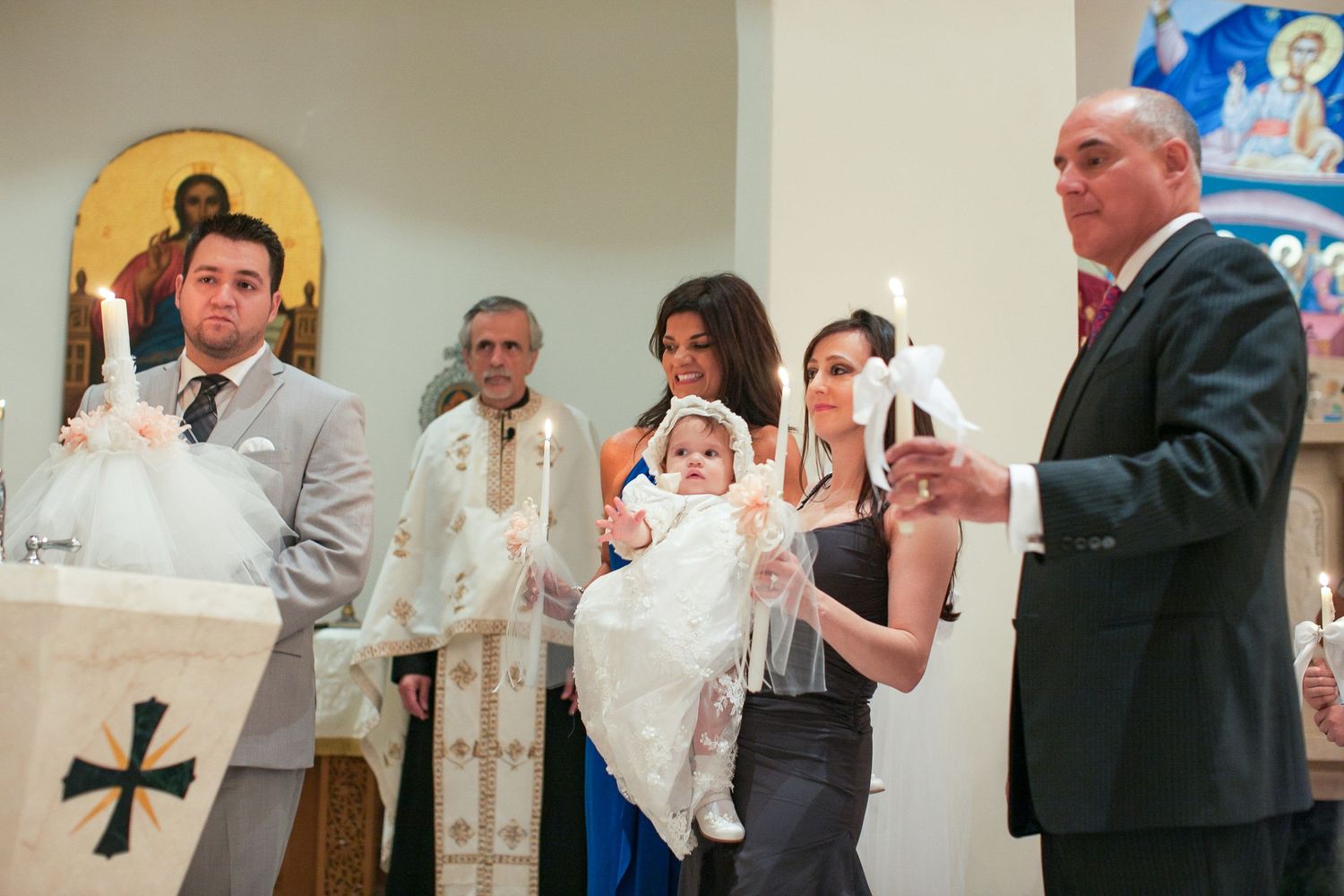 A baby baptism ceremony in a church with family holding candles near the altar.