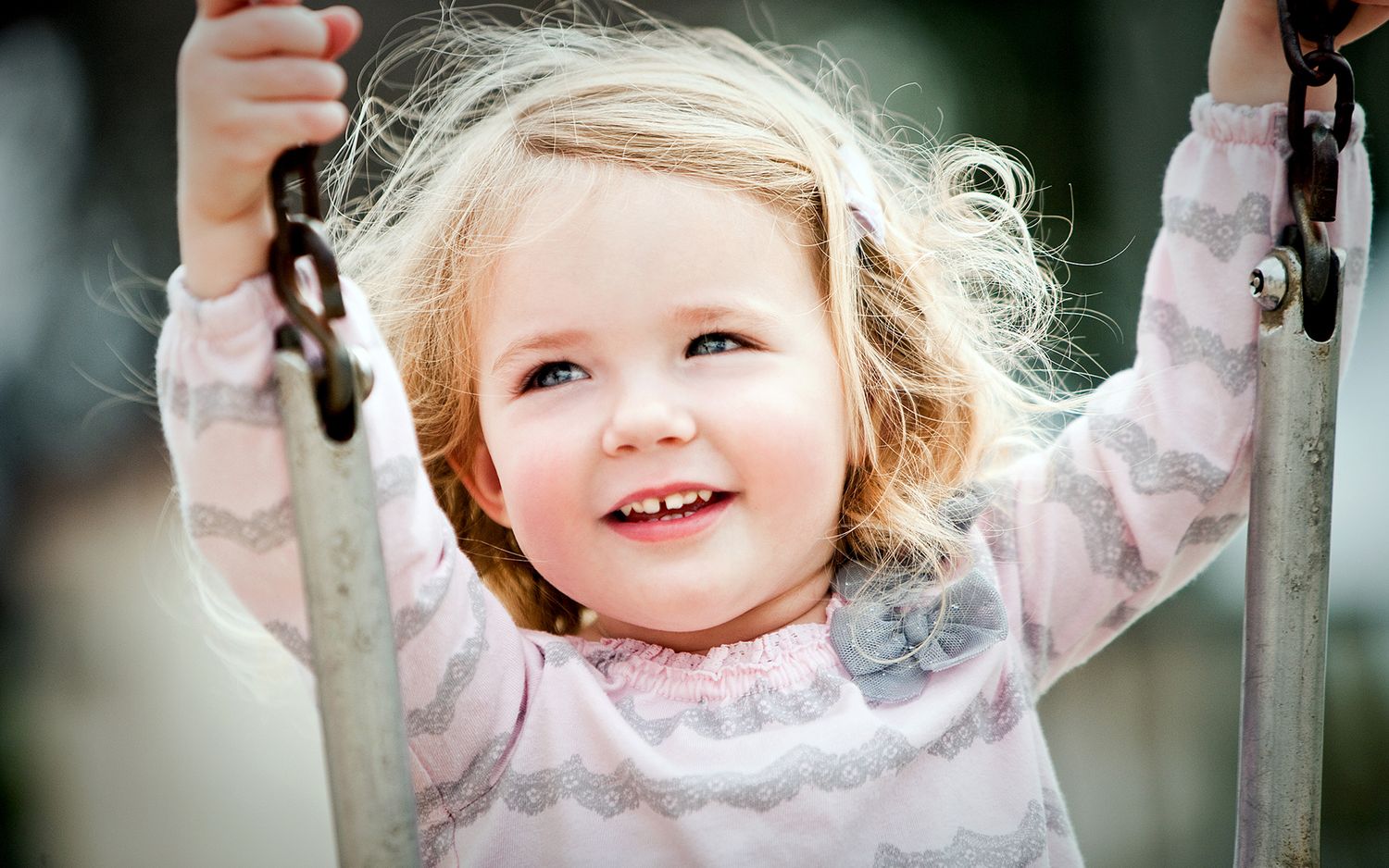 Happy blonde toddler girl smiling while playing on a swing.