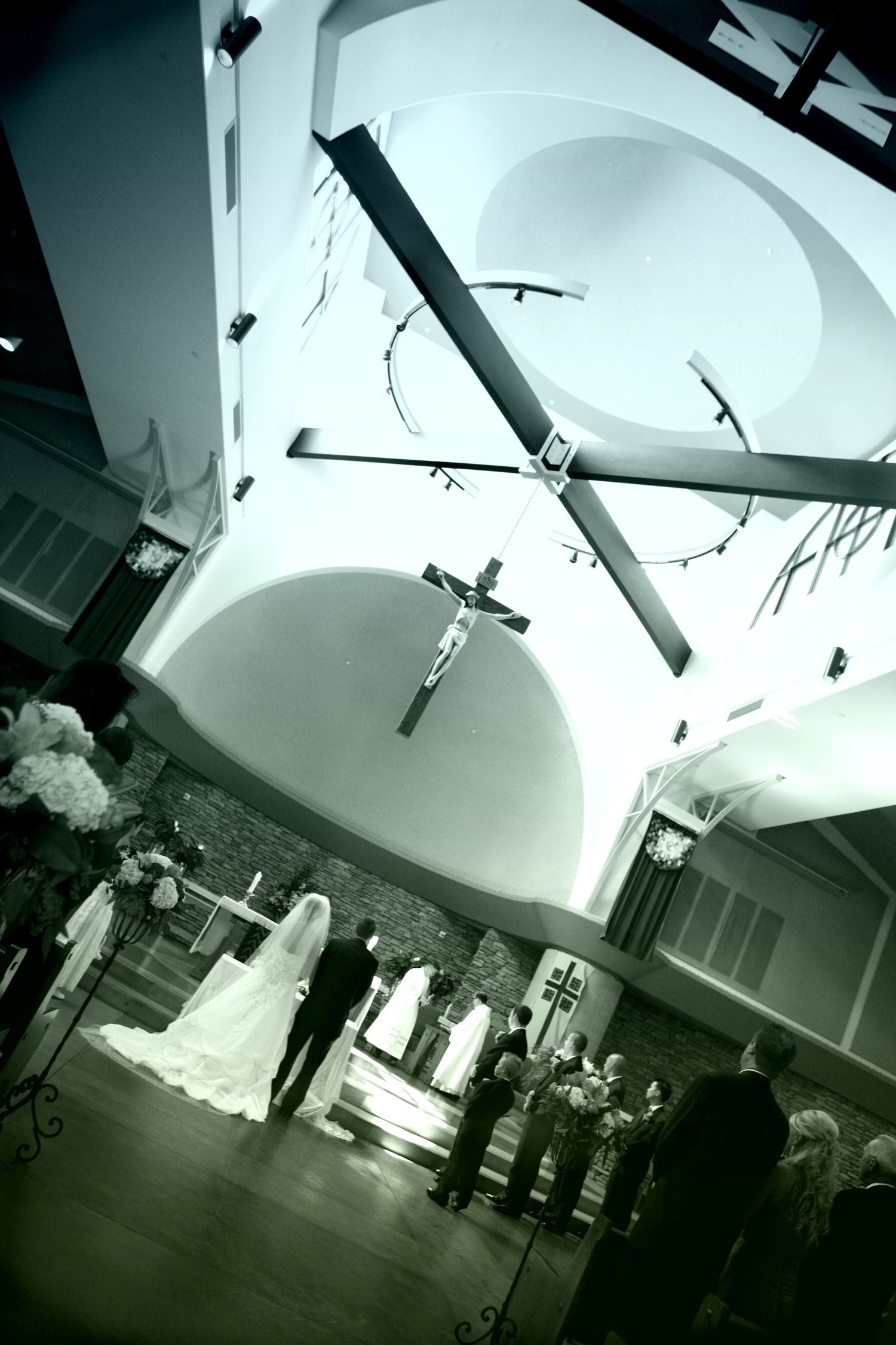 Black and white photo of a wedding ceremony inside a church with a crucifix and large cross hanging from the ceiling.