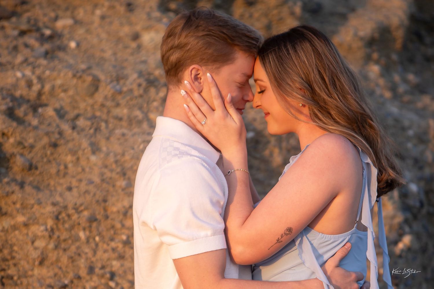Romantic couple touching foreheads tenderly against golden rocky backdrop at sunset.