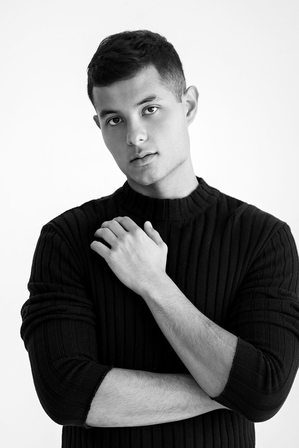 Black and white portrait of a young man in a black turtleneck sweater with arms crossed.