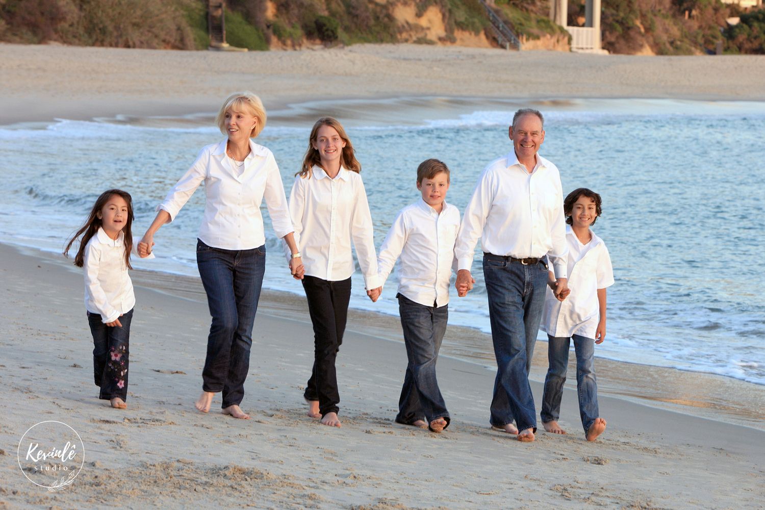 Family of six walking hand-in-hand along a sunny sandy beach together.