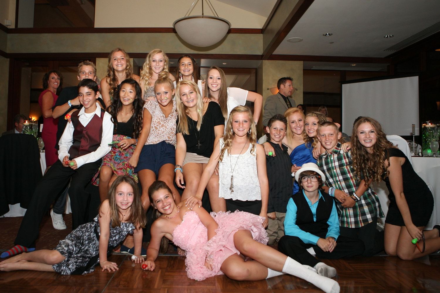 Large group of teenage girls posing together at a formal indoor event, smiling for a group photo.