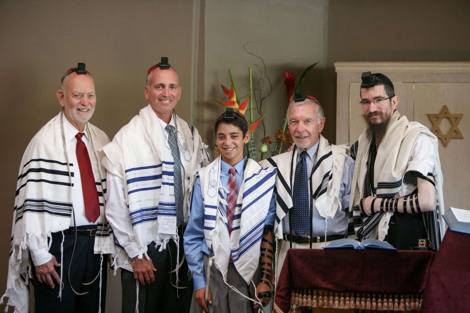 Five men wearing Jewish prayer shawls (tallitot) pose together smiling at a Bar Mitzvah ceremony.