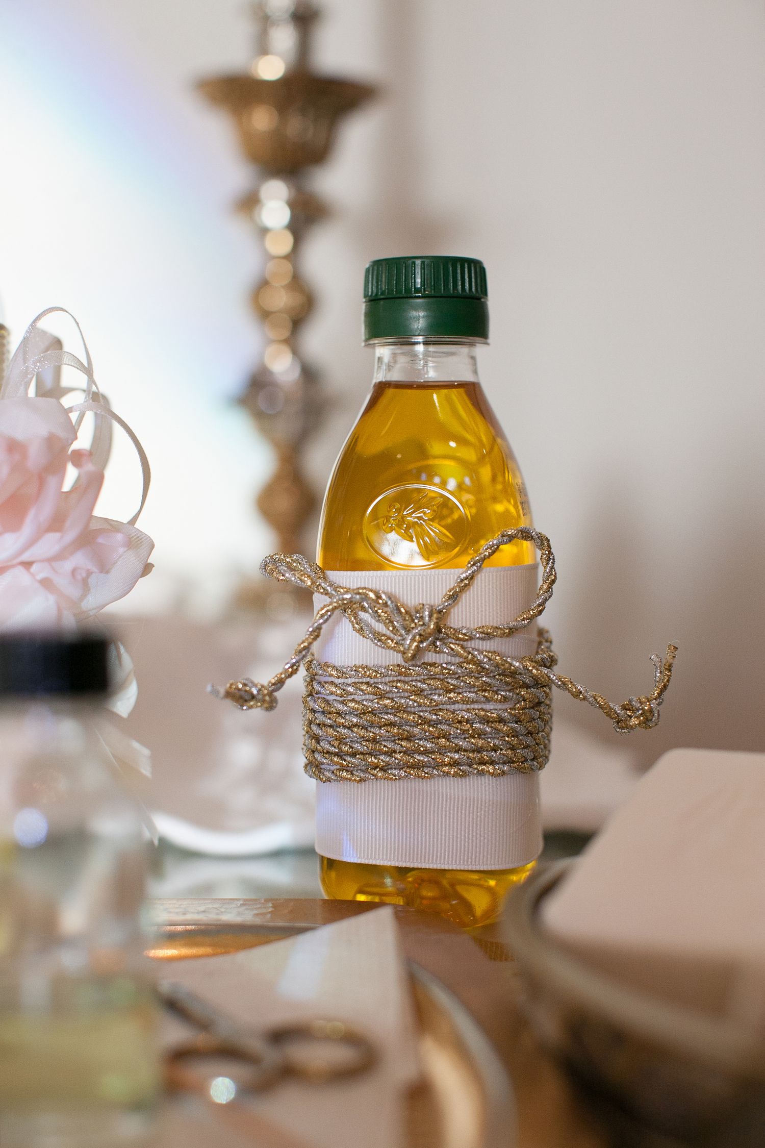 Small plastic bottle of golden oil tied with decorative rope and blank label on reflective surface.