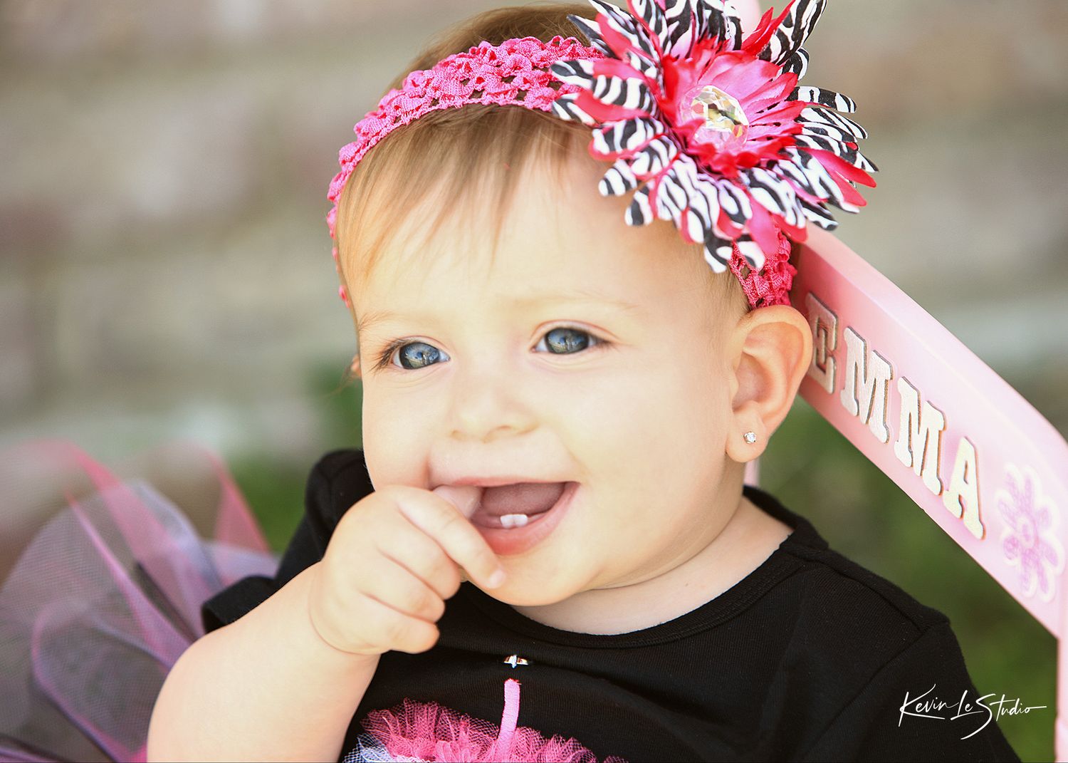 Smiling baby girl with blue eyes wearing pink headband with flower and black shirt with pink tutu.
