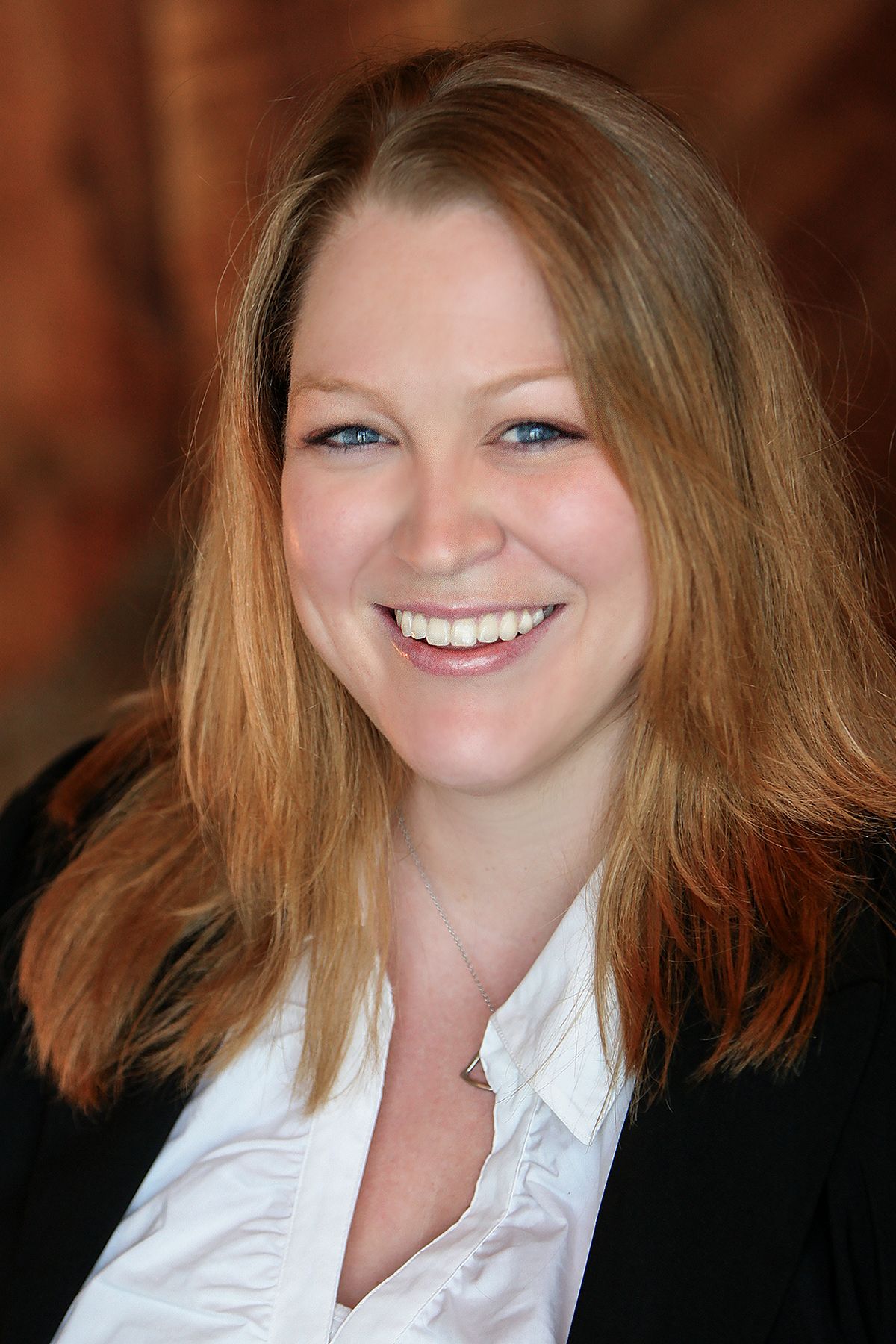 Professional headshot of a smiling woman with long blonde hair wearing a black blazer and white shirt.