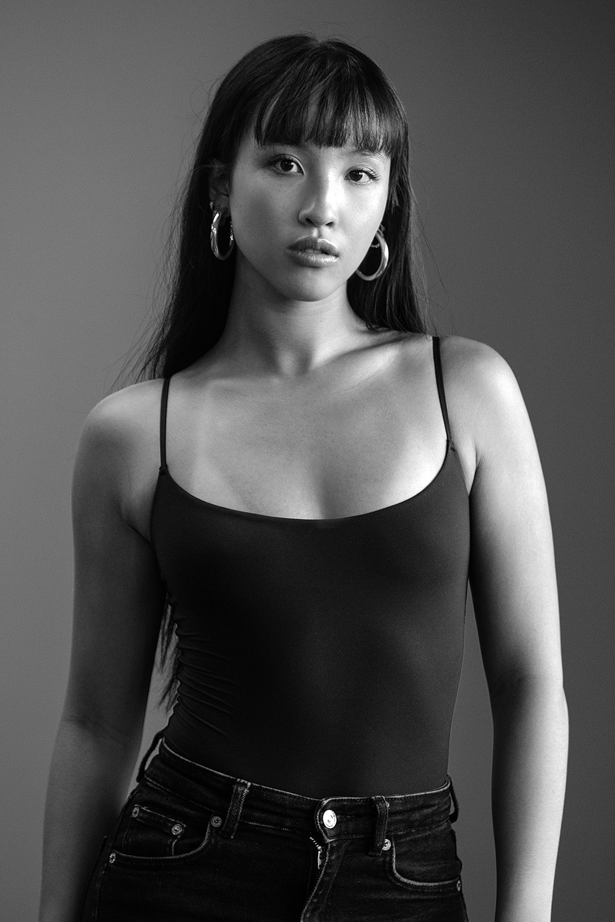 Black and white portrait of a young Asian woman in a black bodysuit with hoop earrings.