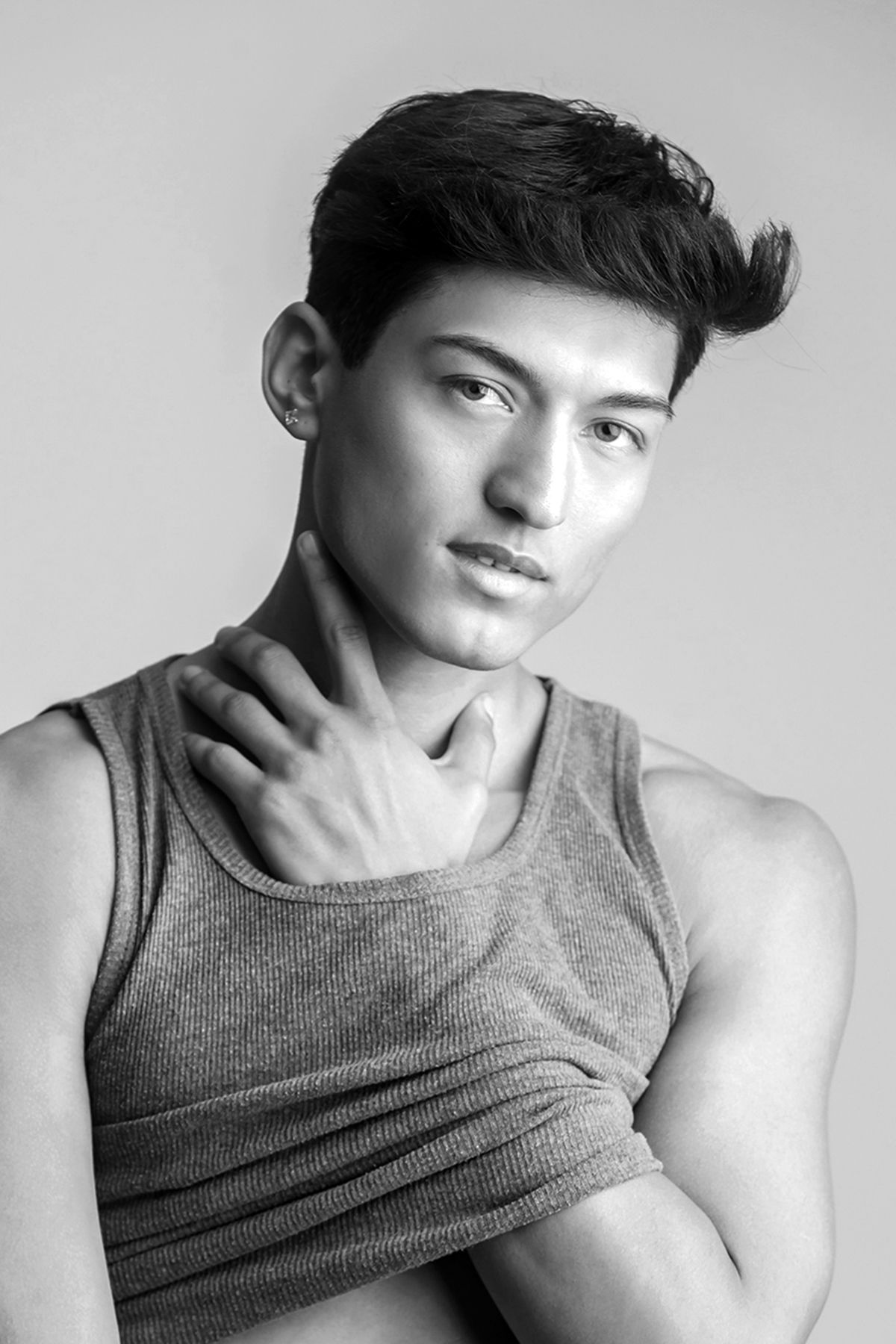 Black and white portrait of a young man in a tank top, posing with hand on shoulder against a light background.