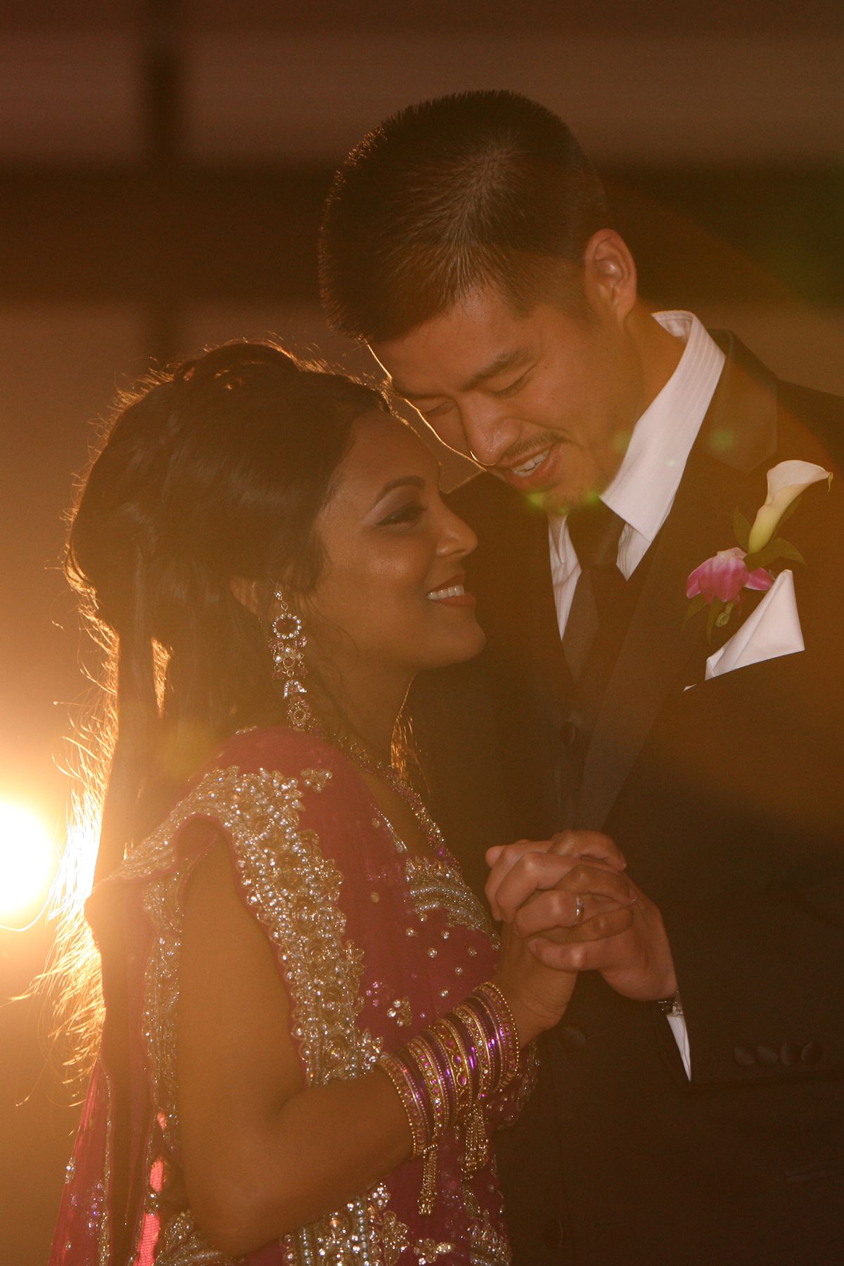 Indian bride in red lehenga dances with groom in black suit at wedding reception.