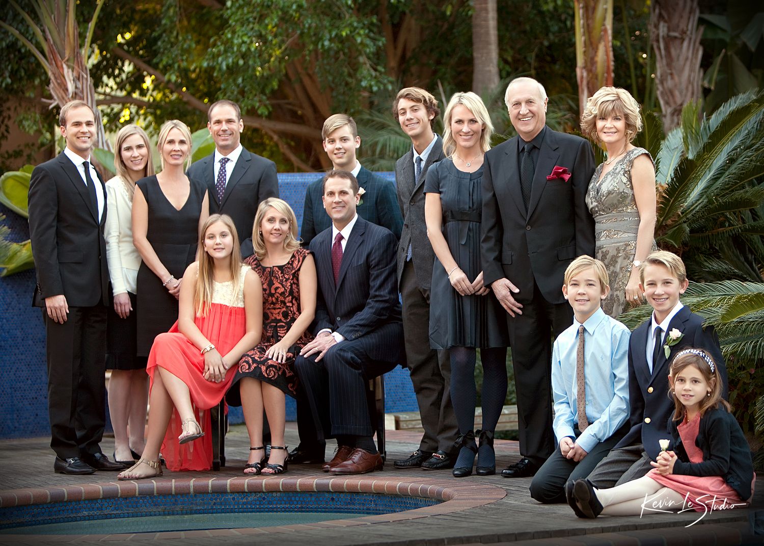 Large family group portrait posed outdoors near a pool, dressed in formal attire for a special occasion.