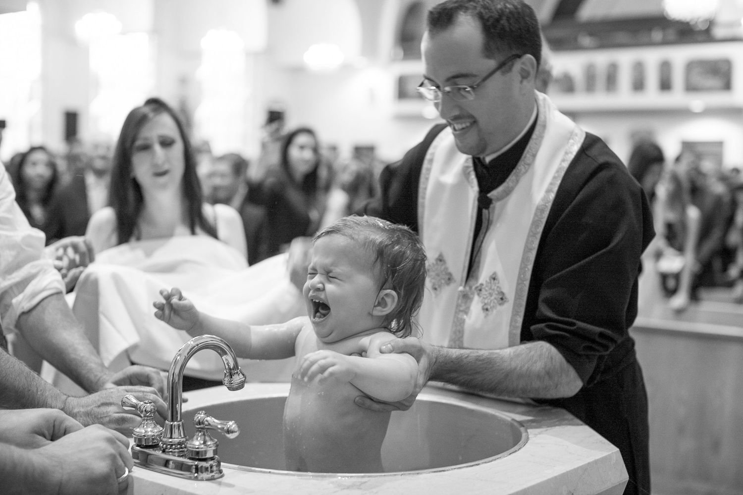 Crying baby during Catholic baptism ceremony with priest in church.