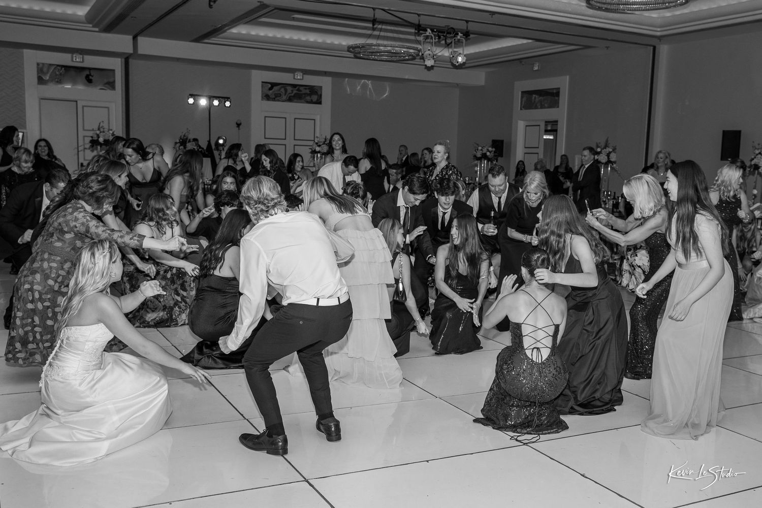 Black and white photo of wedding guests forming a circle on the dance floor during a lively reception celebration.