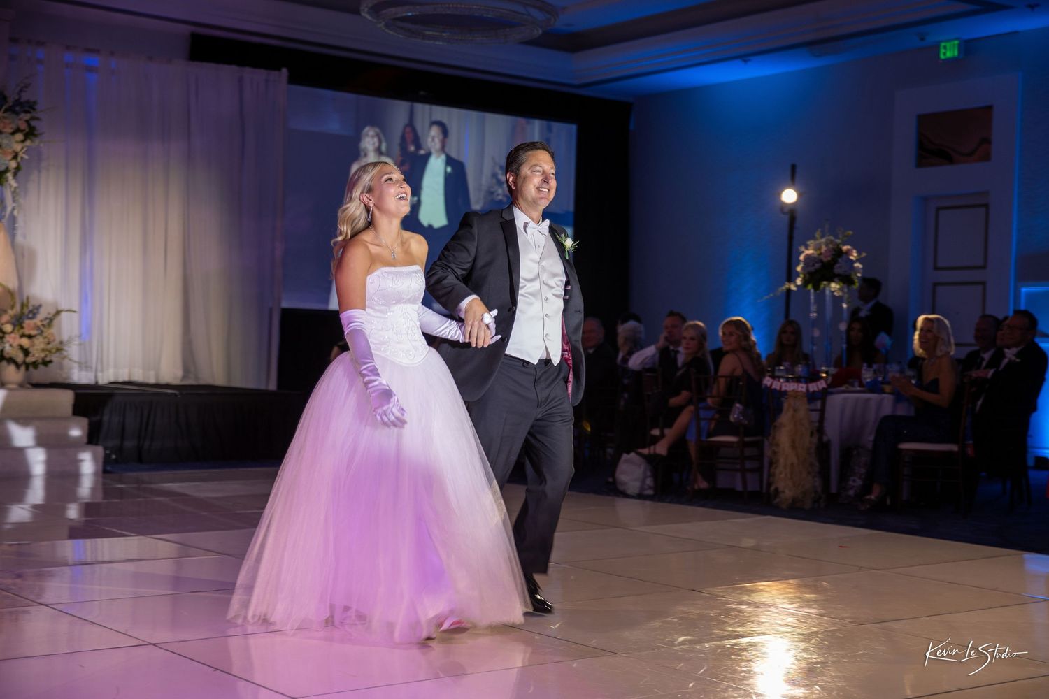 Bride in pink ball gown and groom in tuxedo share their first dance at elegant wedding reception.
