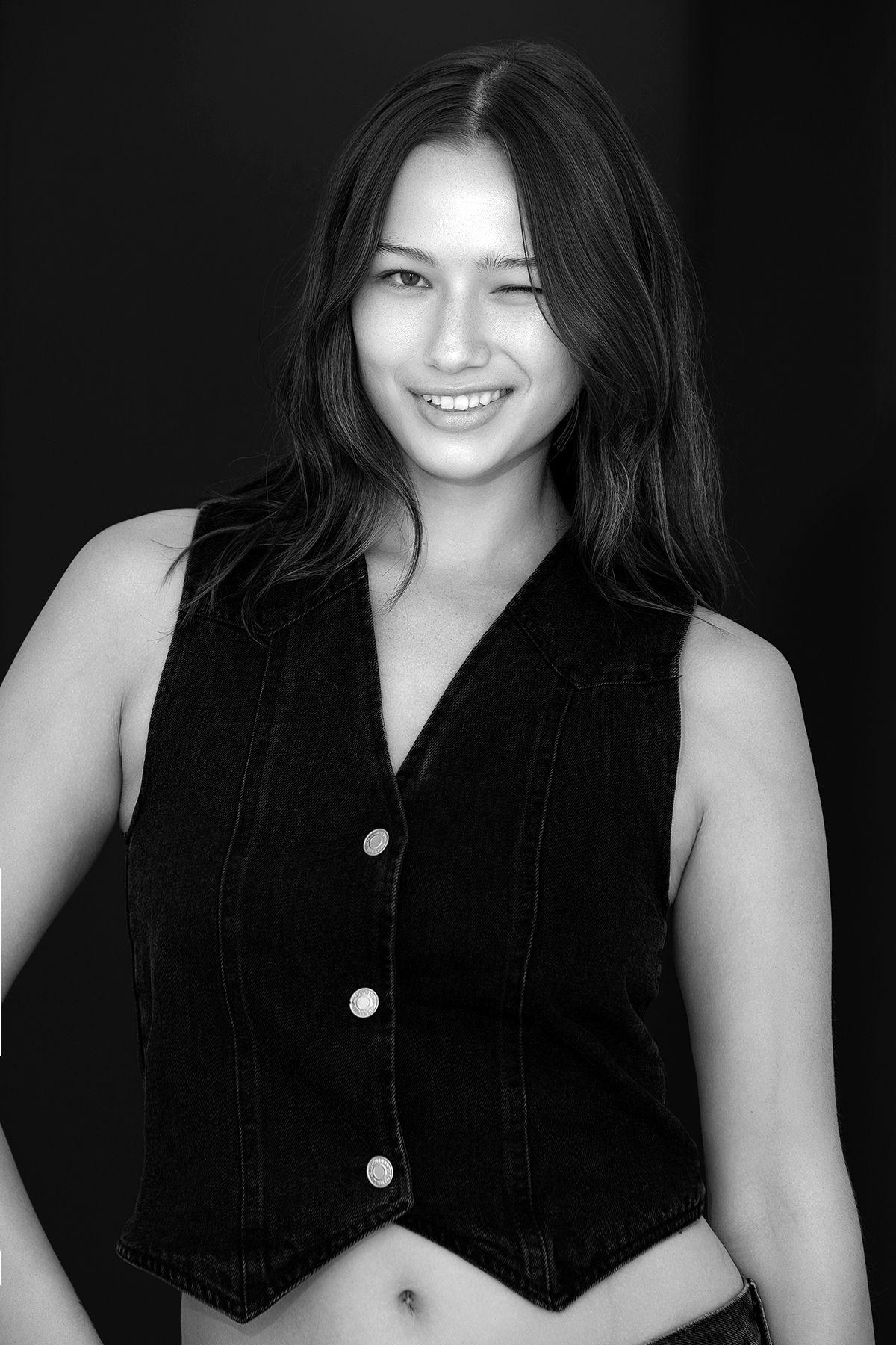 Black and white portrait of a smiling young woman with long hair in a denim vest.