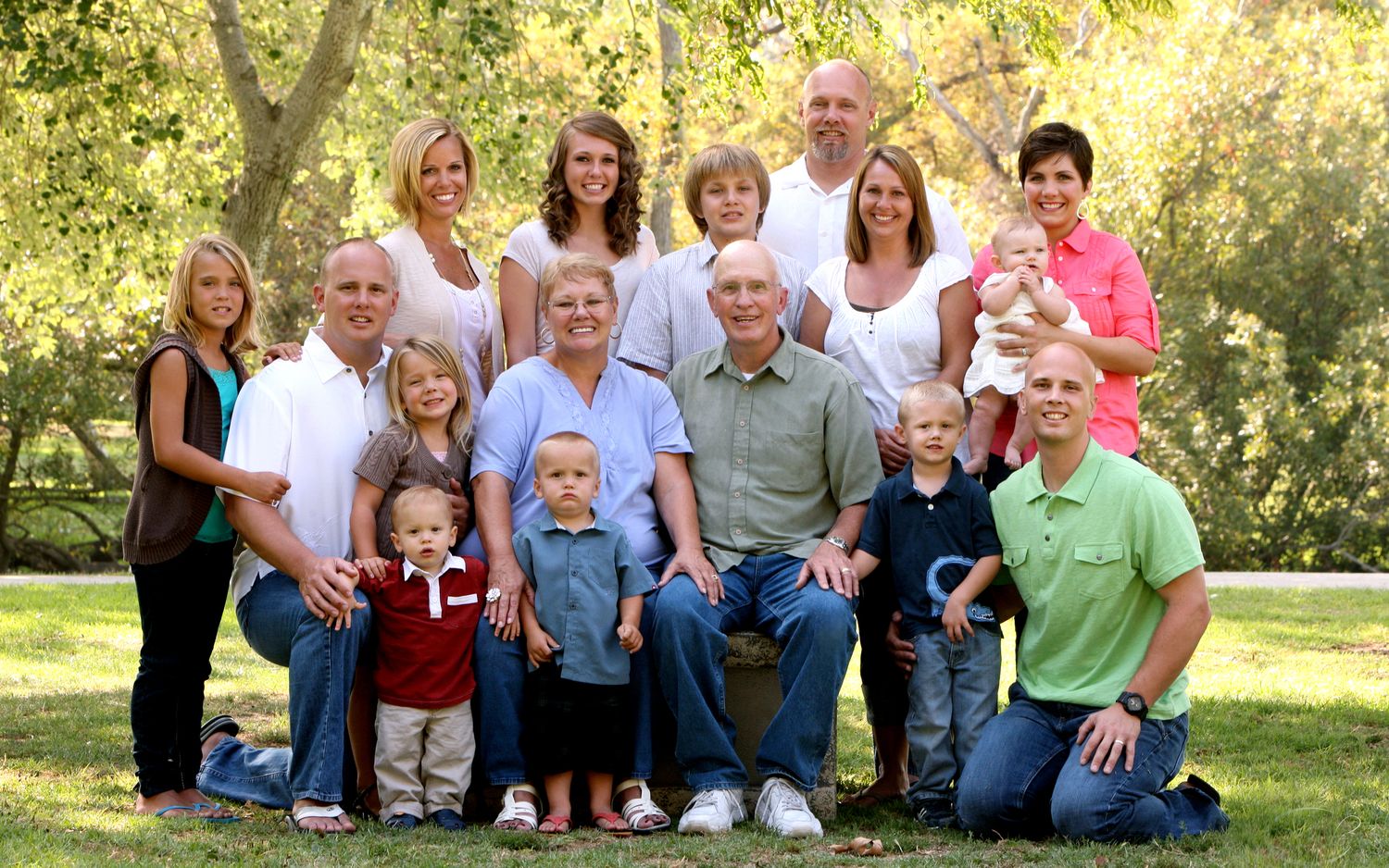 Large multigenerational family group portrait outdoors in a lush green park setting.