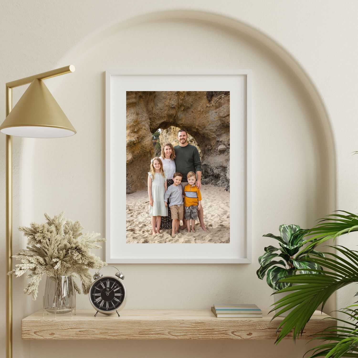 Framed family photo print displayed on a shelf in a bright home, featuring parents and children posing on a sandy beach.