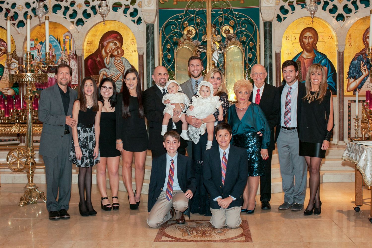 Family group portrait inside ornate Greek Orthodox church with golden icons, gathered for a baptism ceremony.
