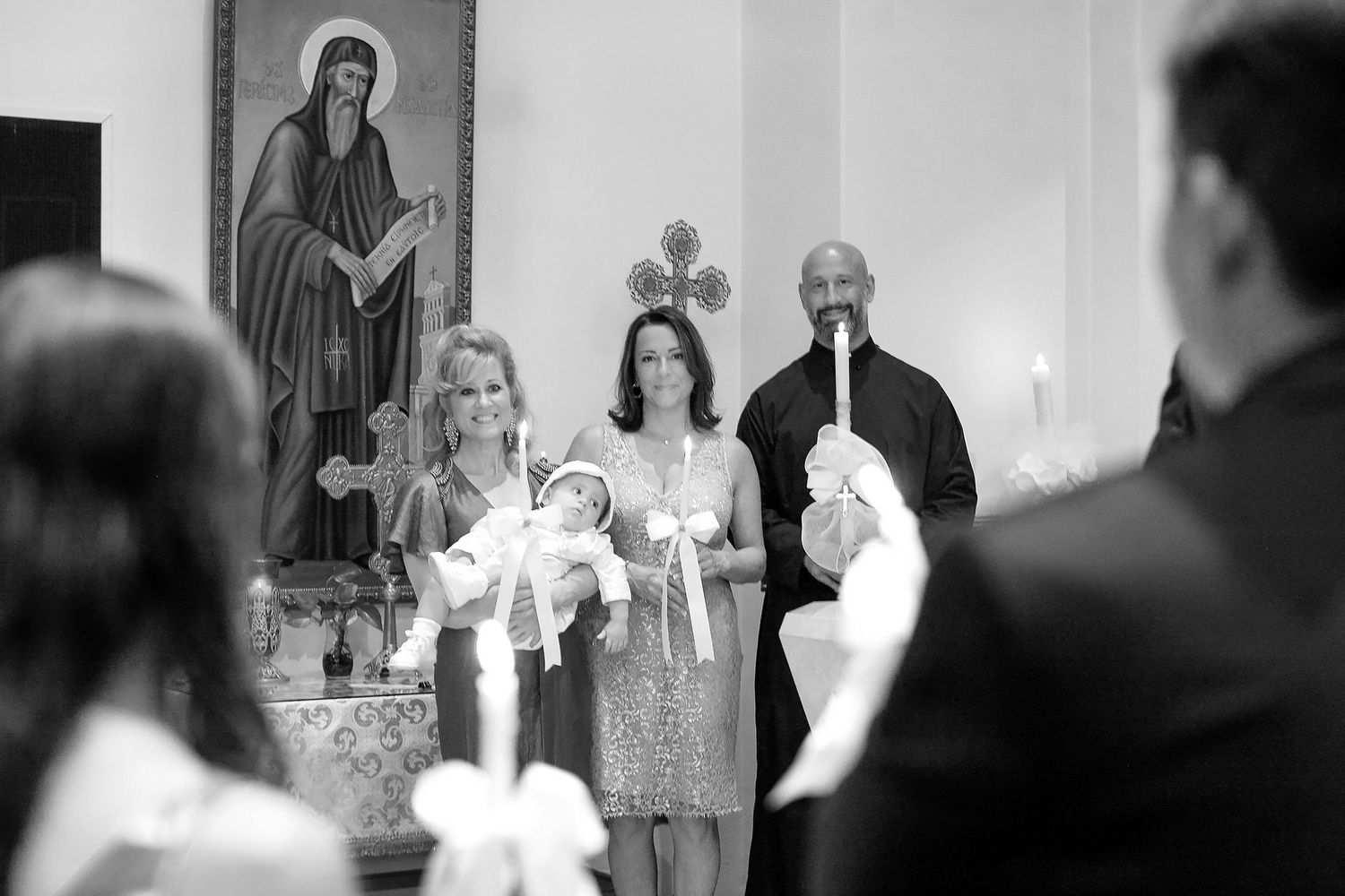 Black and white photo of a baptism ceremony with godparents holding a baby in a church.
