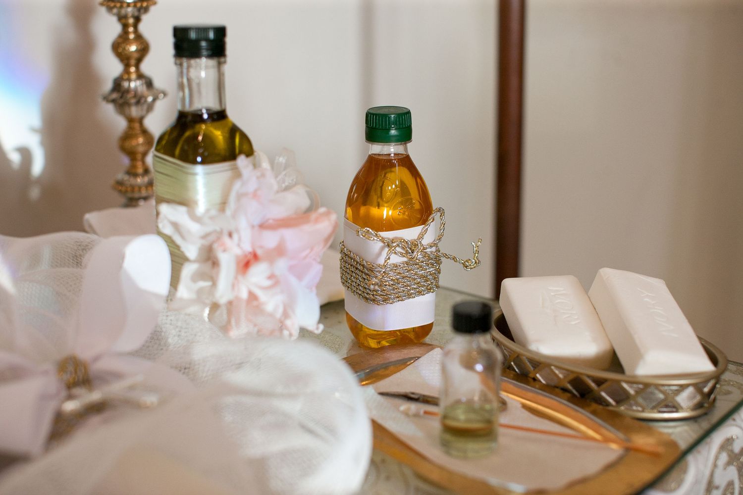 Elegant table display with olive oil bottles, decorative ribbon, white soap bars, and pink flowers for a wedding ceremony.