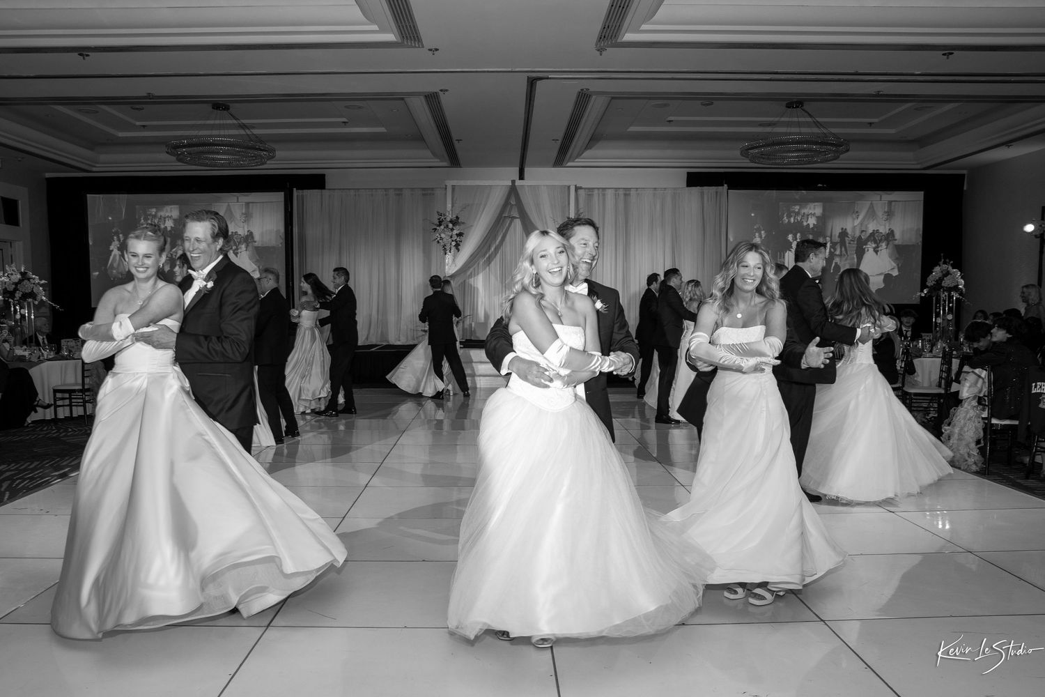 Black and white photo of bridesmaids and groomsmen dancing elegantly on a white dance floor at a wedding reception.