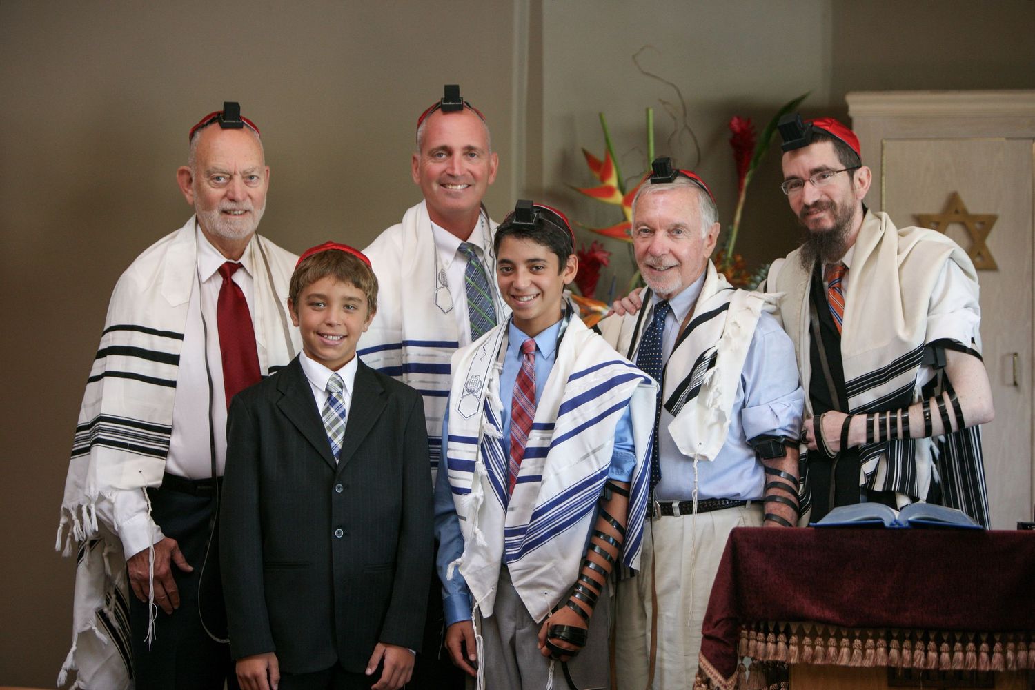 Group of men and boys in Jewish prayer shawls posing together at a Bar Mitzvah celebration.
