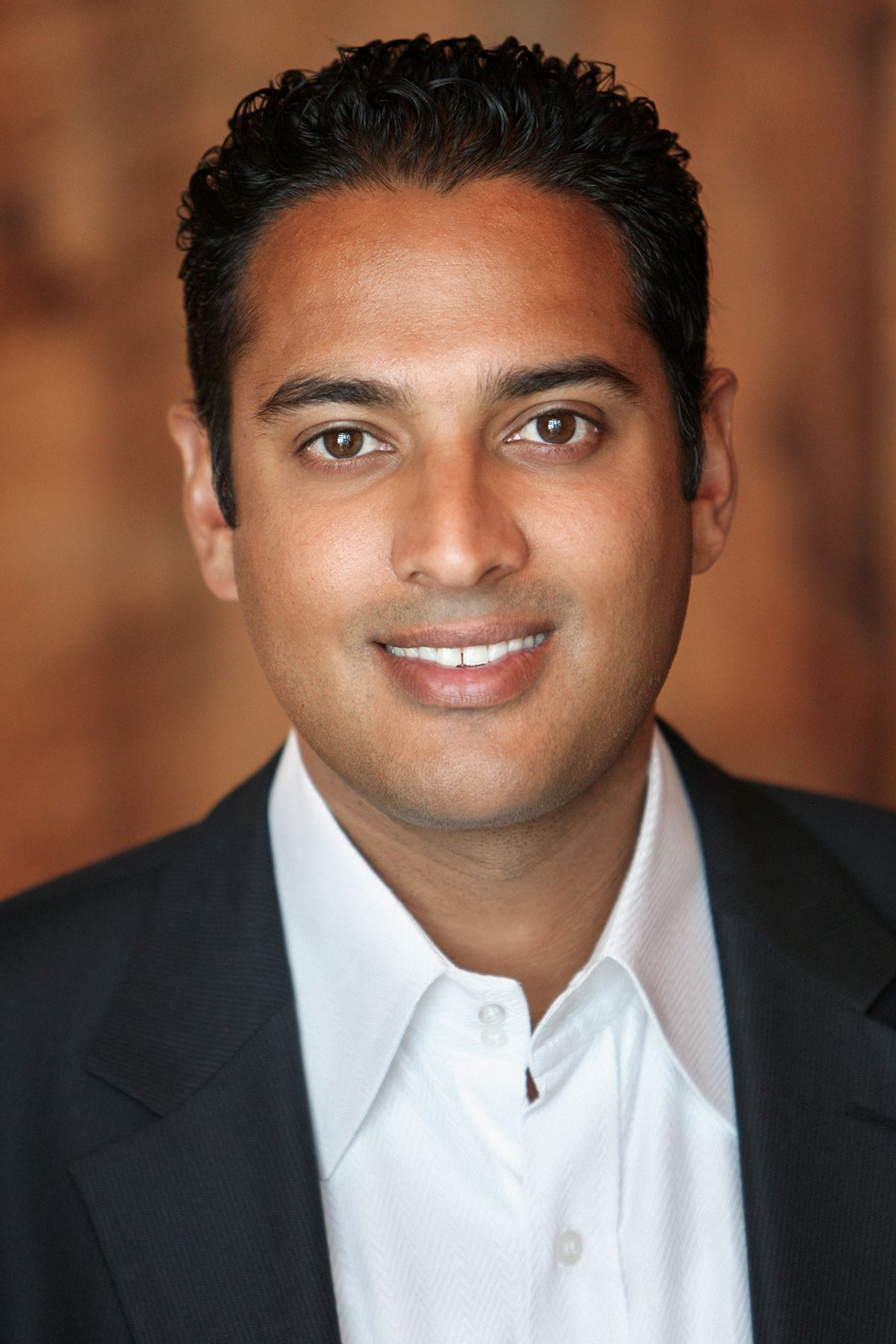 Professional headshot of a smiling man with dark hair wearing a dark blazer and white dress shirt.