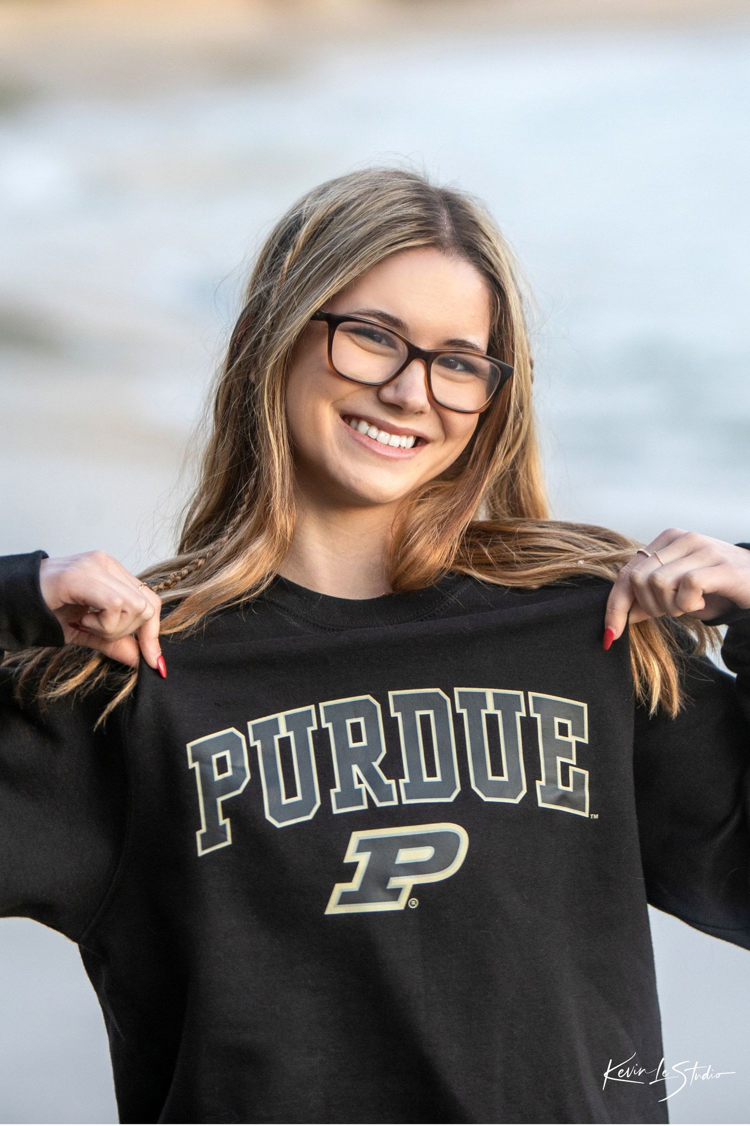 Smiling blonde girl holding up a Purdue University sweatshirt at the beach.