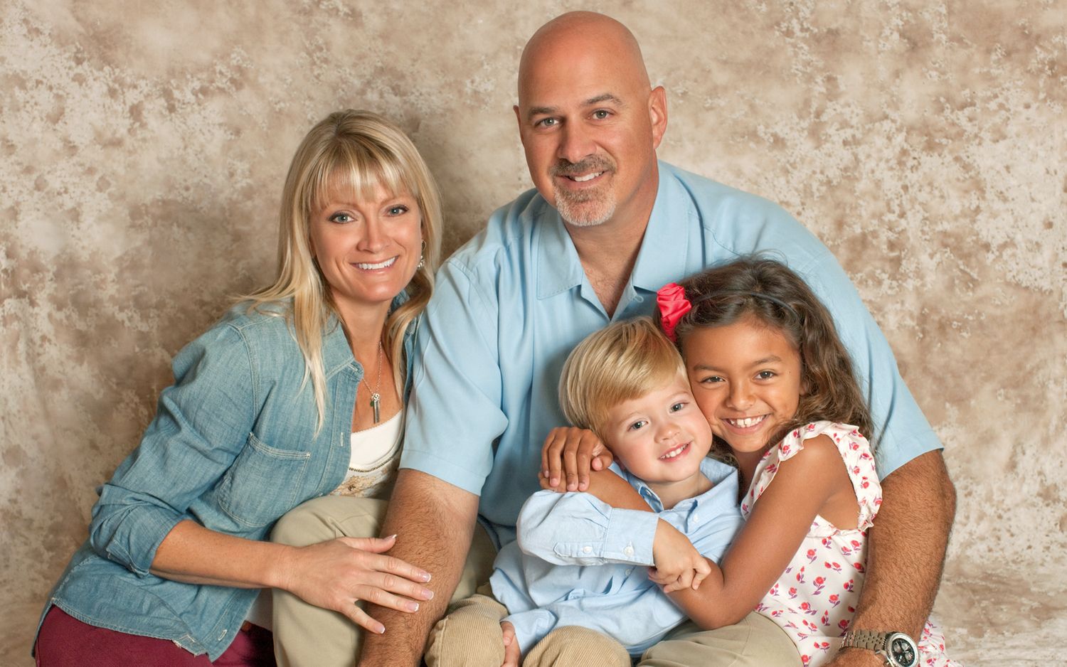 Smiling family of four posing together for a warm studio portrait with two young children.