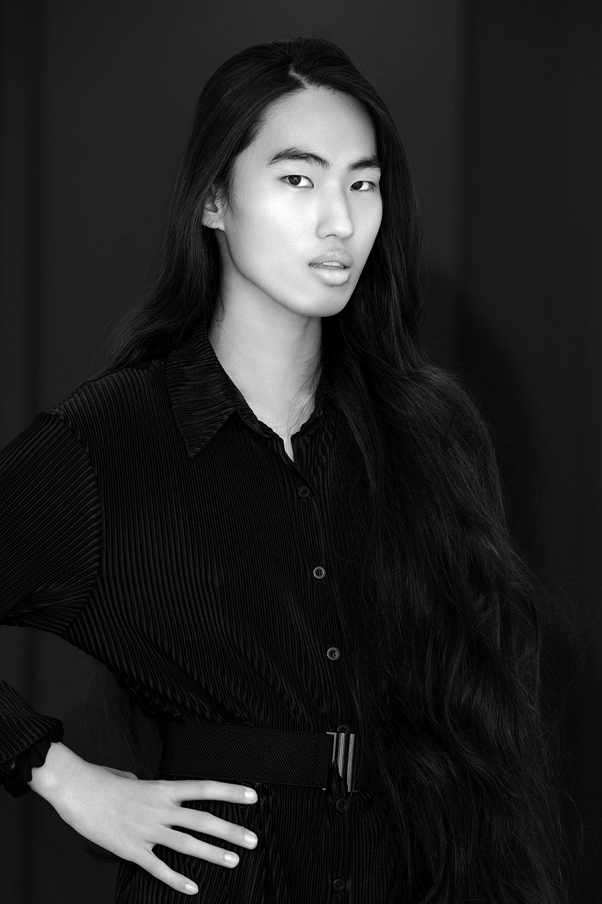 Black and white portrait of an Asian man with long wavy hair in a black striped shirt.
