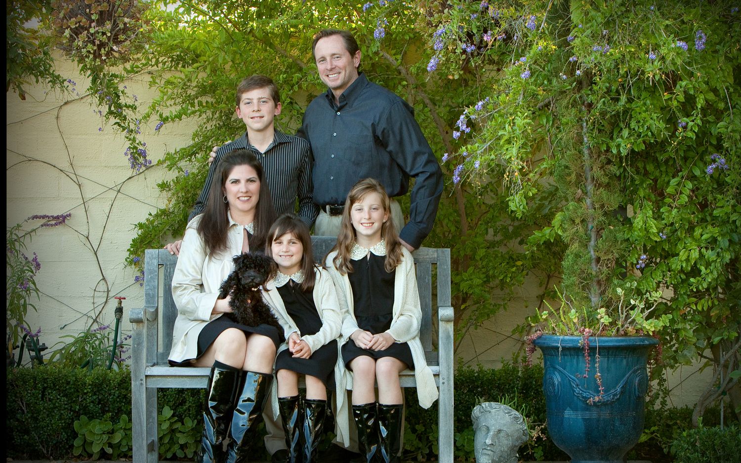 Family of five with dog posing on garden bench surrounded by lush greenery.