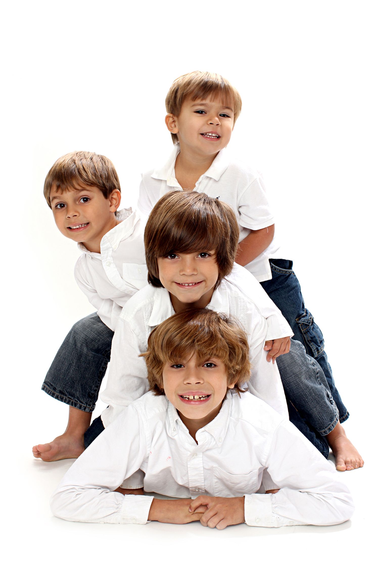 Four young boys in white shirts and jeans pose together in a playful stack formation against white background.