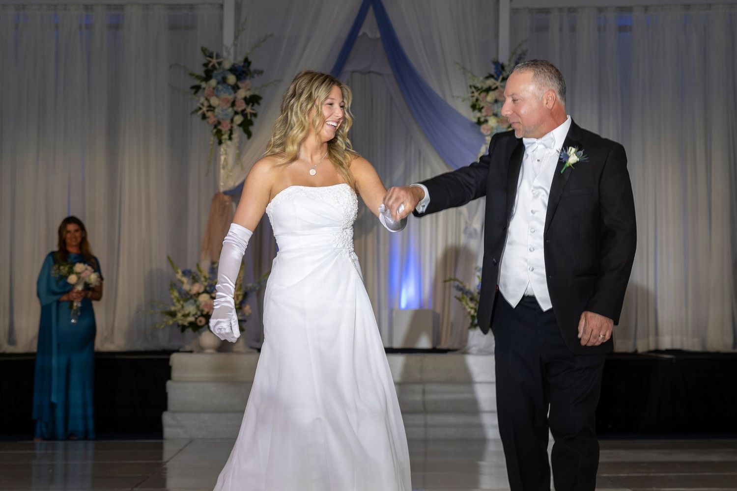 Bride in white gown and gloves shares first dance with groom in tuxedo at elegant wedding reception.