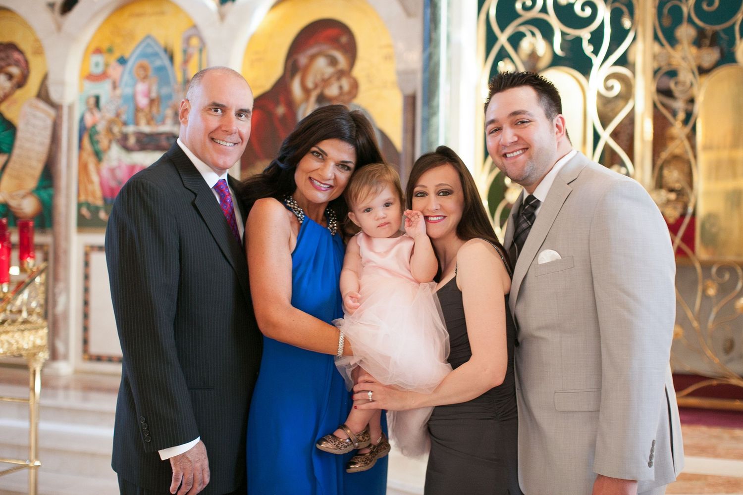 Family of five posing together in an ornate church, with a woman holding a baby girl in a pink dress.