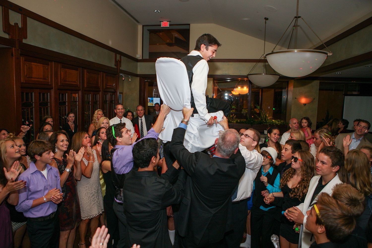 Groom lifted by guests during lively Jewish wedding hora dance celebration in elegant reception venue.