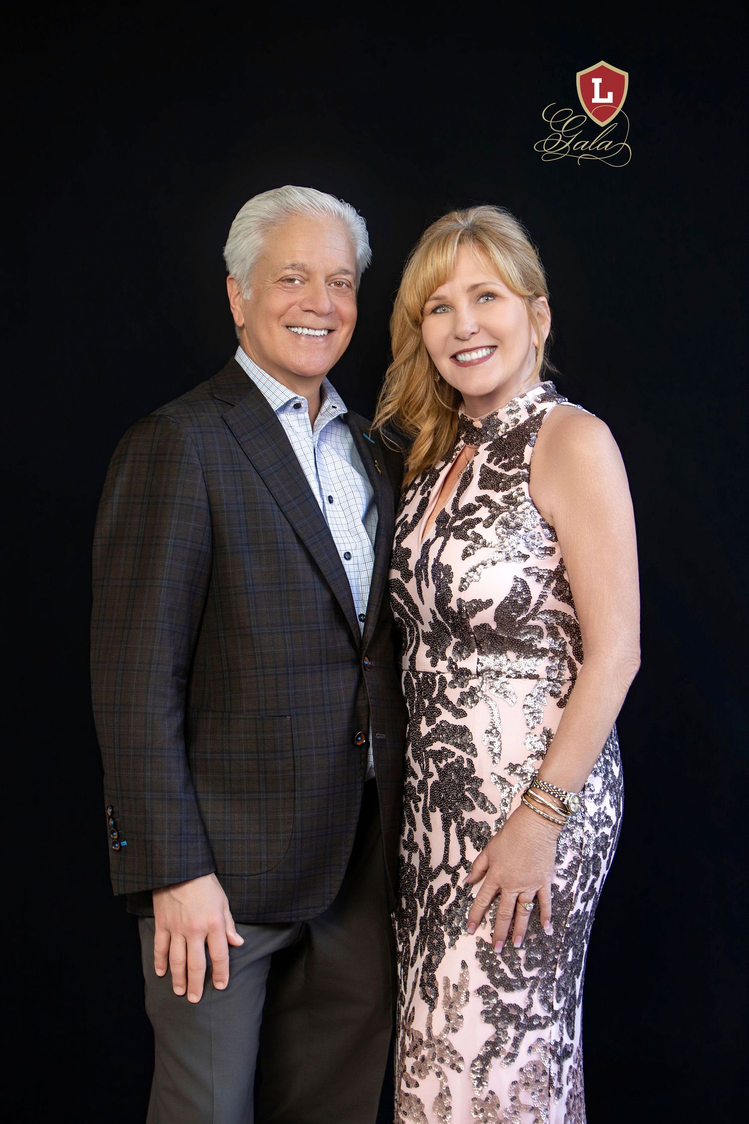 Smiling couple posing at a formal gala event, man in dark blazer and woman in elegant sequined gown.