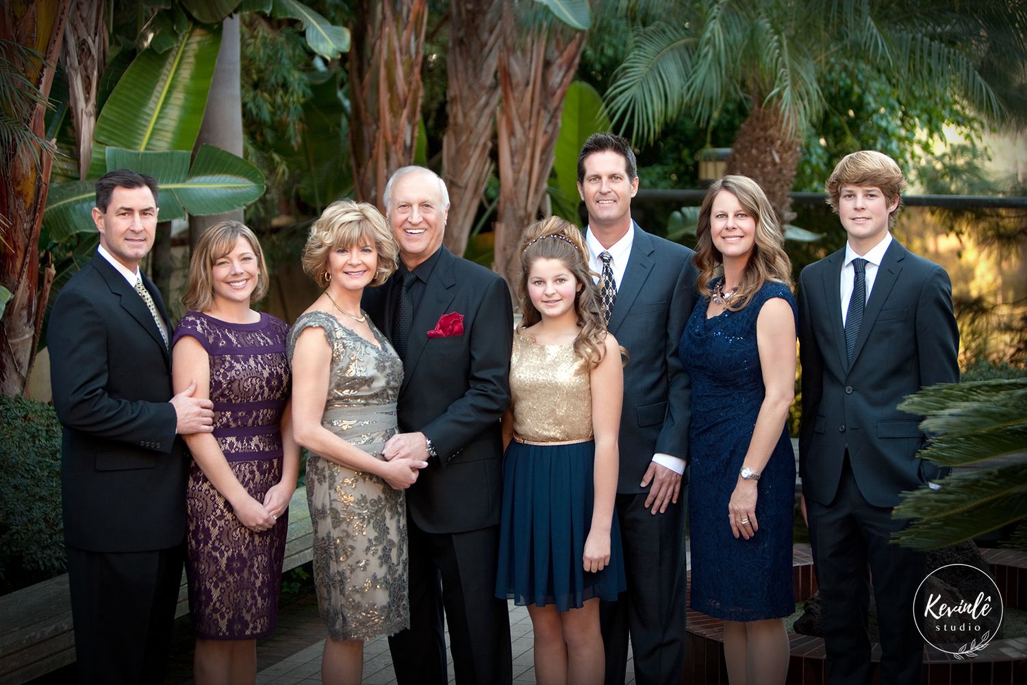 Elegant extended family of eight posing formally in a lush garden setting.
